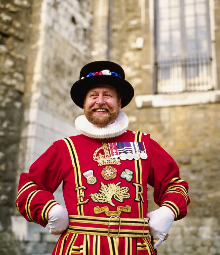 Image of yeoman warder guard at Tower of London, wearing the famous bright red uniform and black hat, with a big smile