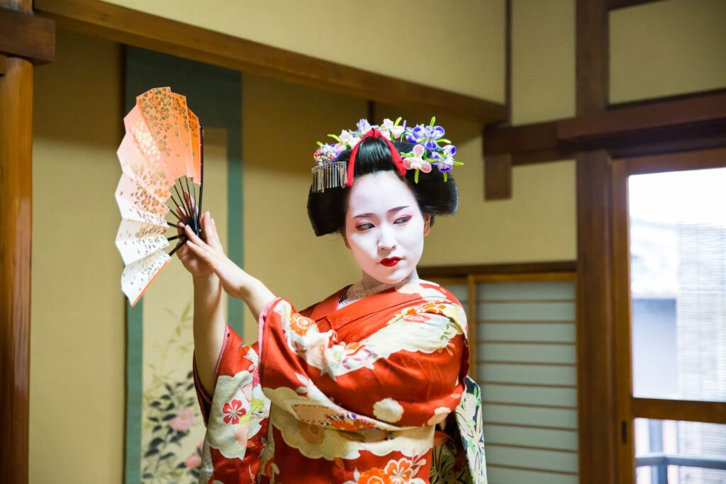 Image of Geisha Maiko girl dancing with a traditional paper fan in Japanese tatami room