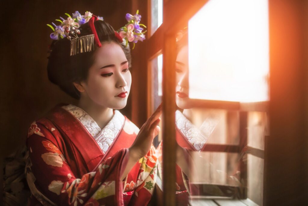 Image of young geisha in Kyoto looking out of a window, wearing traditional make up and kimono