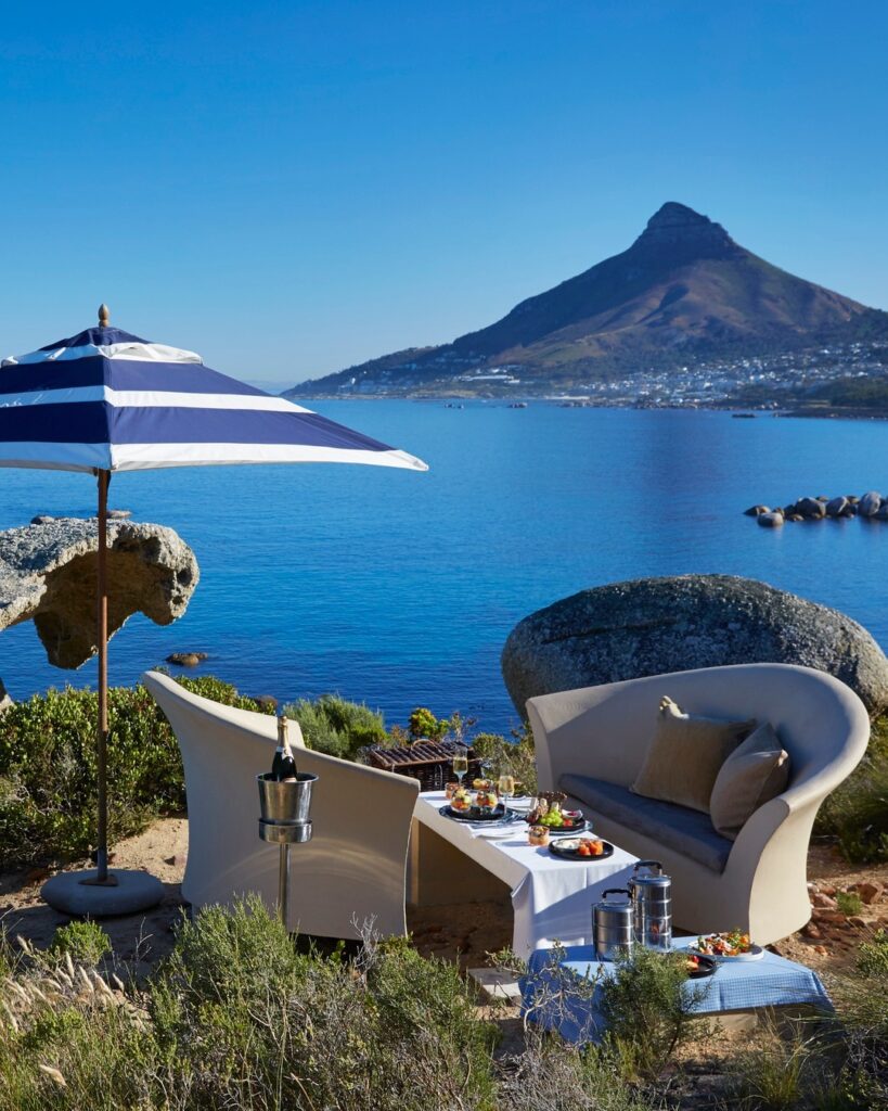 Image of an outdoor picnic, set up overlooking the calm ocean with a blue and white-striped parasol for shade