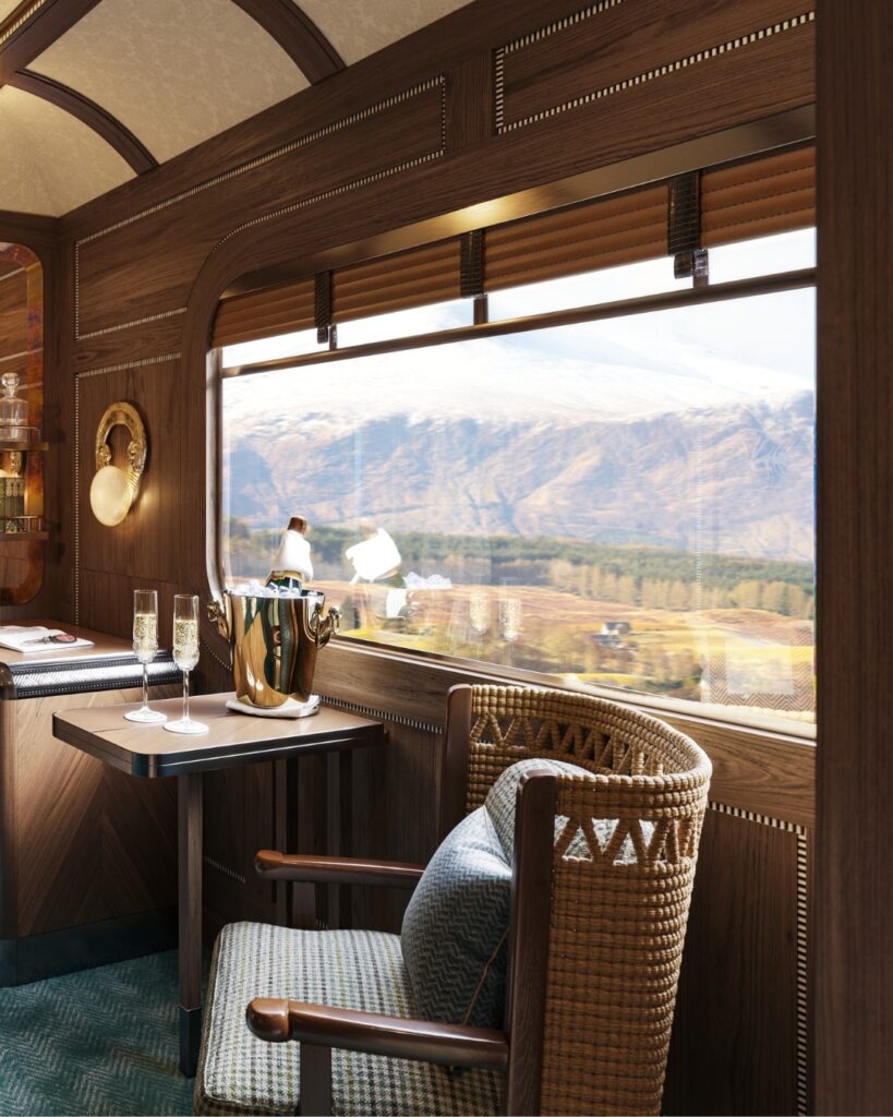 Image of Grand Suit aboard the Royal Scotsman train, with elegant chair and table with champagne glasses and the scenery in the background framed by the window