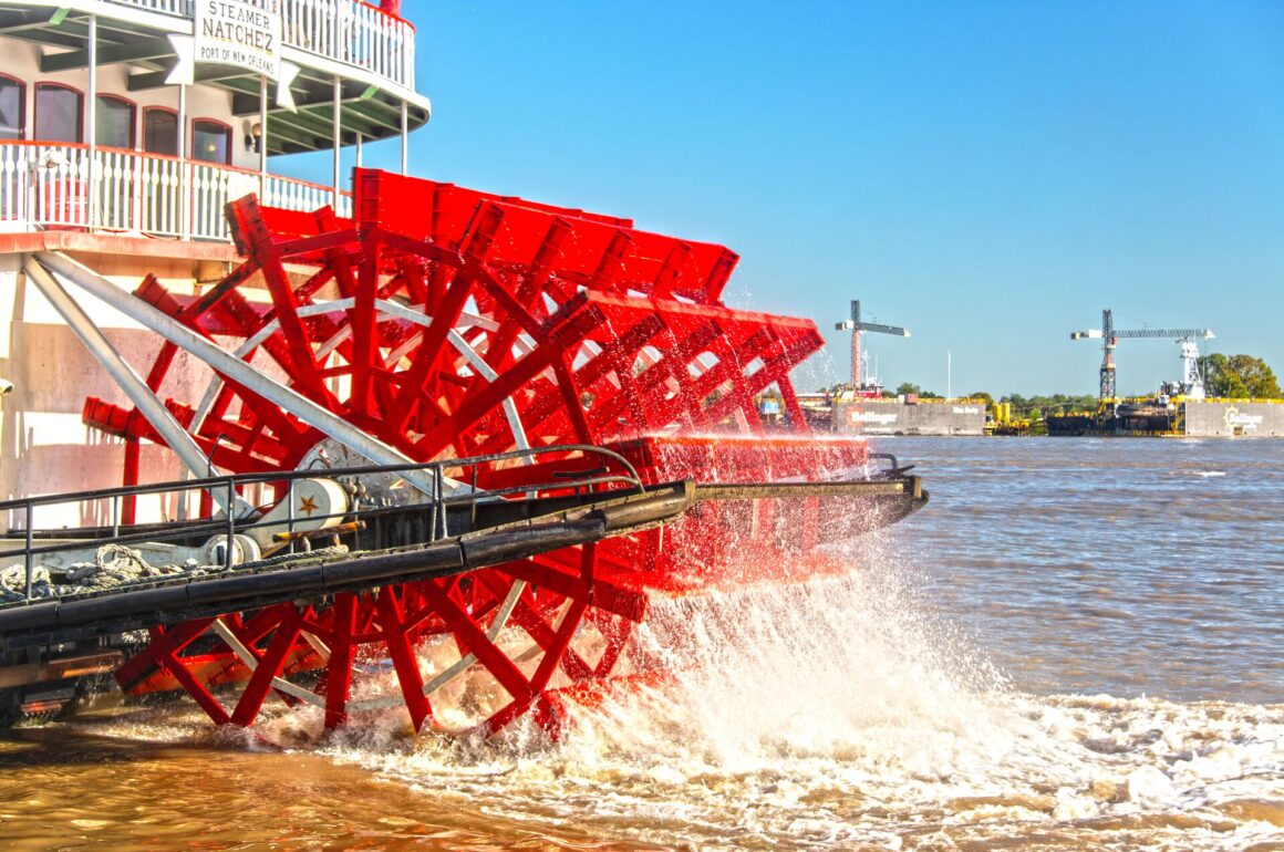 Image of paid boat on the Mississippi Delta, with a bright red wheel and the city in the background