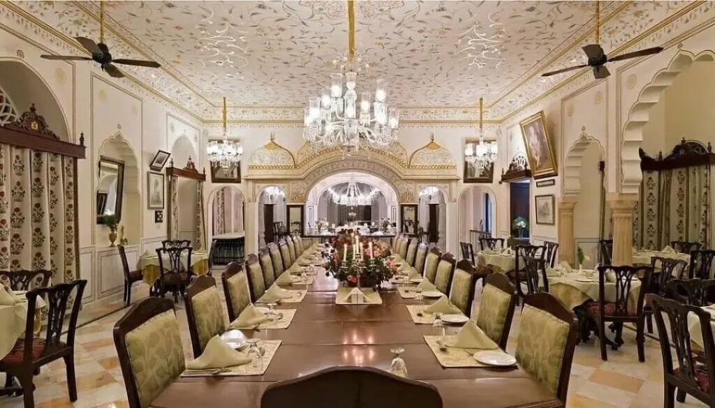 The Grand Dining Hall at the Nahargarh Ranthambhore hotel, showing plush furnishings, rows of chairs and a grand table under a chandelier.