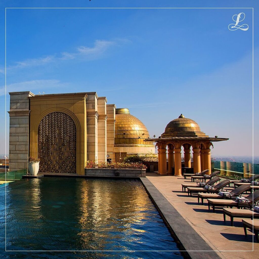 Infinity pool at The Leela Palace hotel New Delhi glistening in the sun with ornate golden buildings in the background