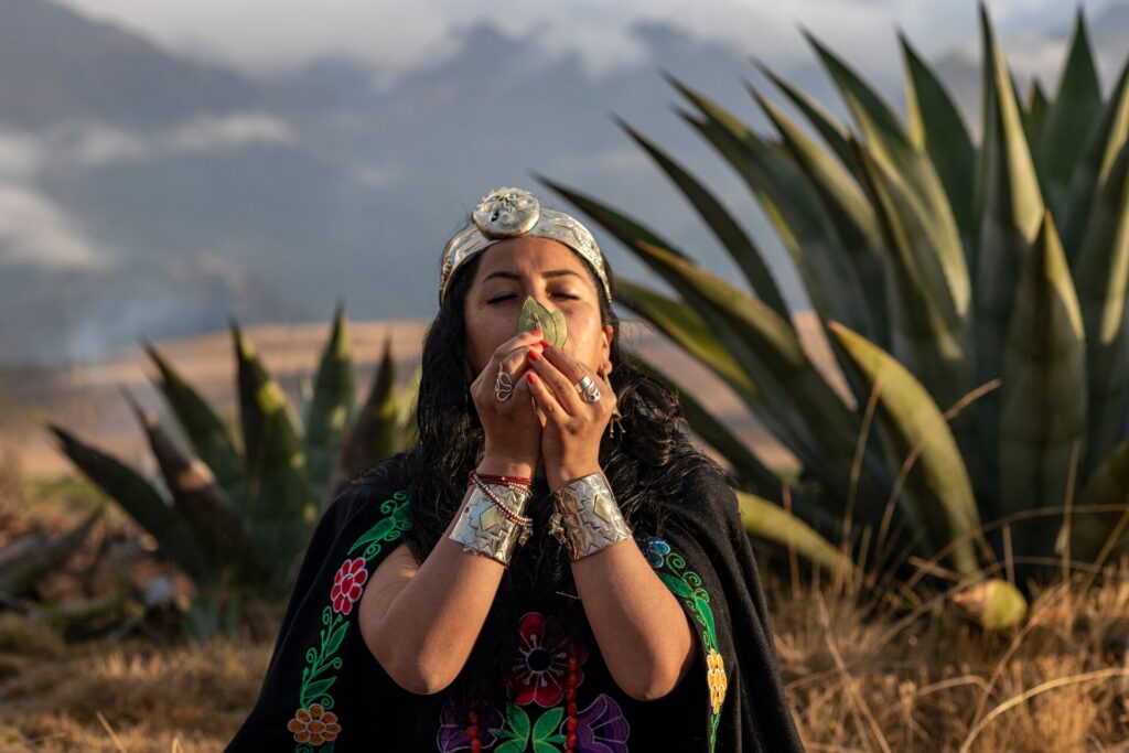 Shaman Laura with her hands up to her face, holding and offering, with the Peruvian mountains behind her 