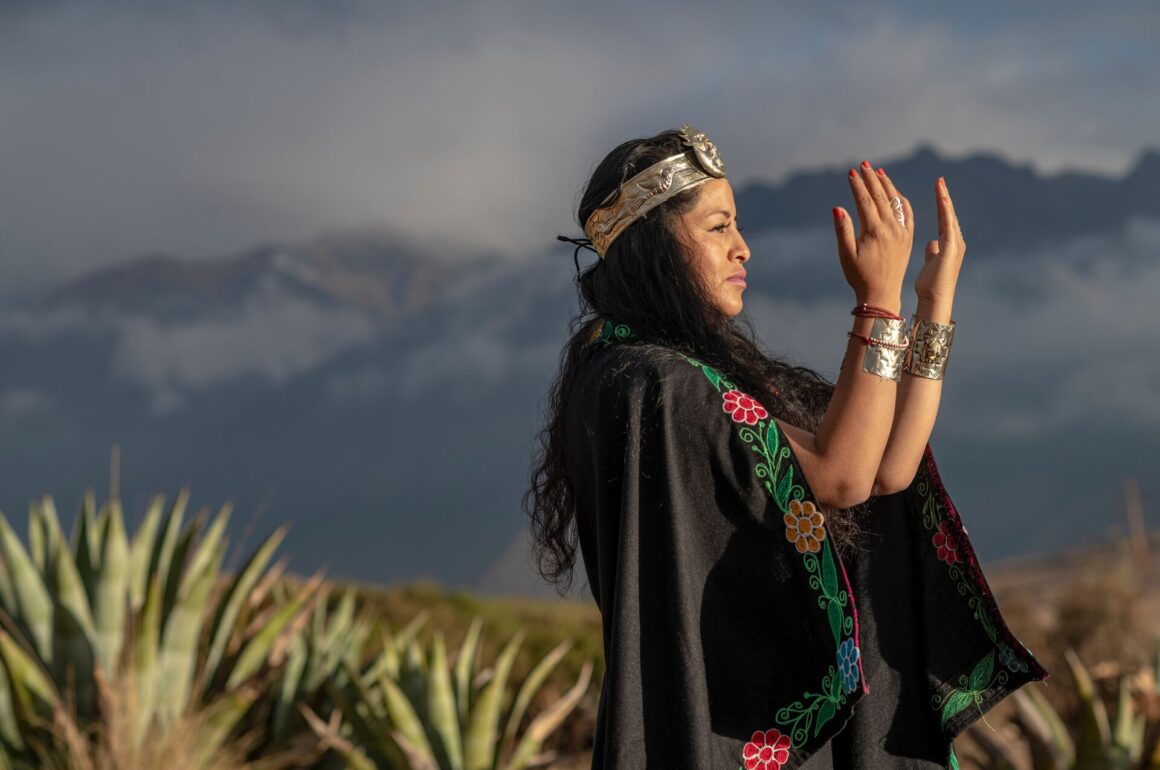Image of Shaman practicing Incan spirituality, in traditional dress with a crown and bracelets against an Andean backdrop
