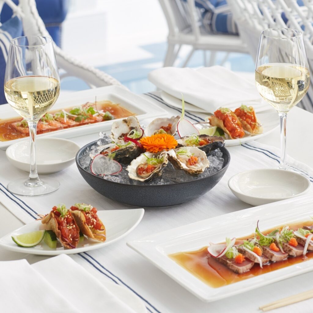 delicate colourful sushi dishes placed on a white table cloth, with high end cutlery and glasses of champagne