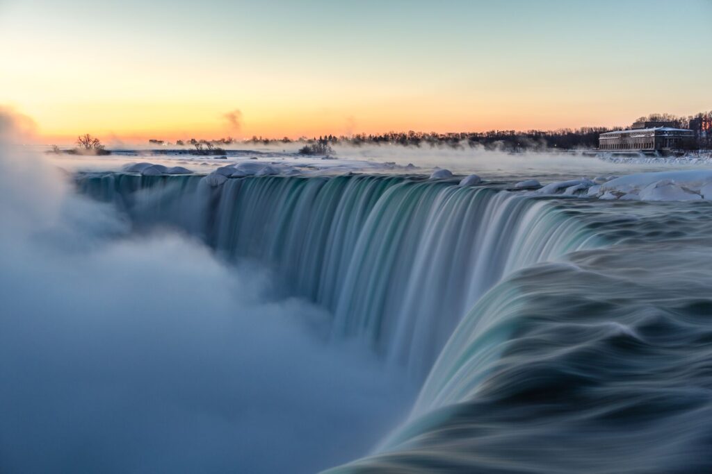 The grey waters of Eastern Canada’s Niagara Falls cascades down, as the sun sets in the sky behind