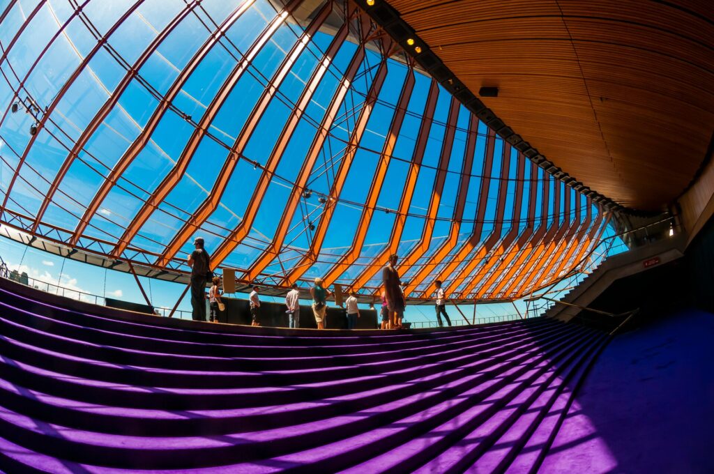 View from under the sails of the Sydney Opera House, with a purple carpet and brown slats with the bright blue sky behind