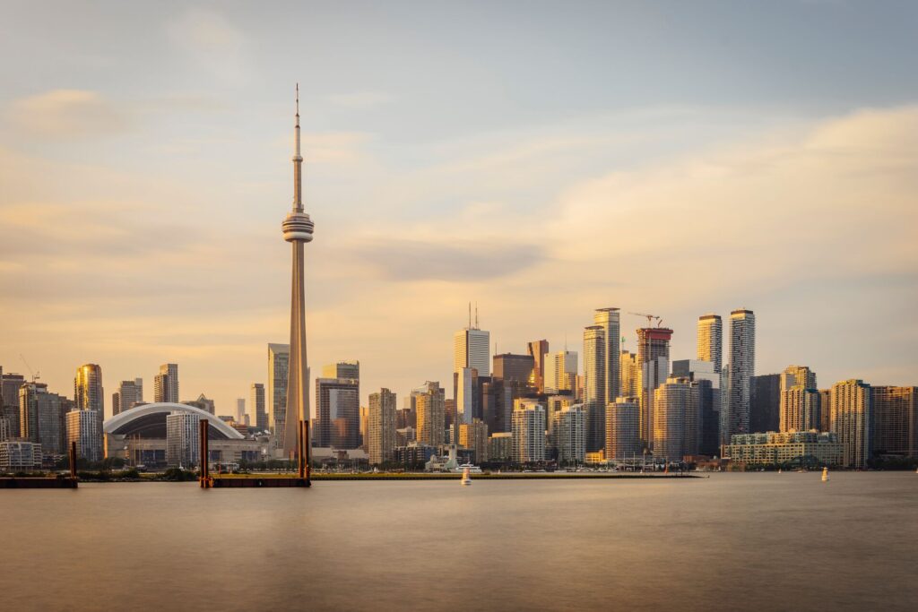 The skyline of Toronto with the CN tower central is pictured with a light tan and grey hue, almost melting into the river in front and sy behind. 