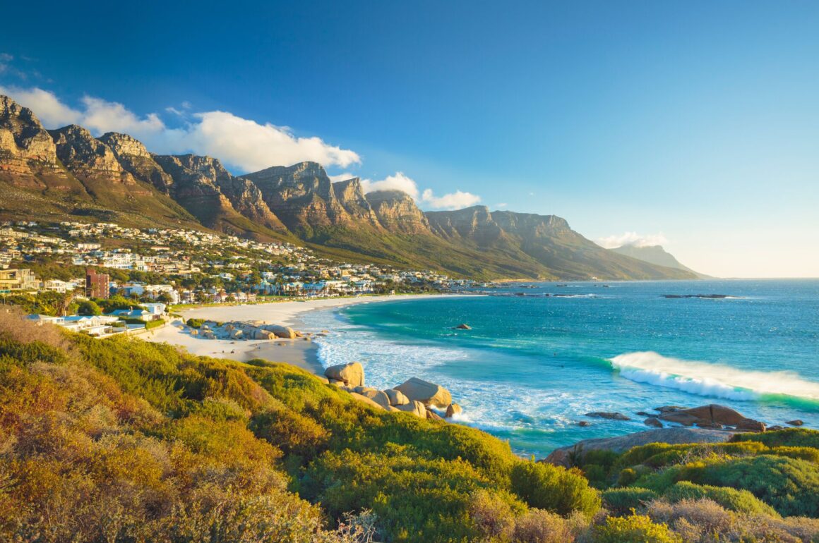 Bright blue se encases by a beach and the Twelve Apostles mountains looking down covered with greenery.