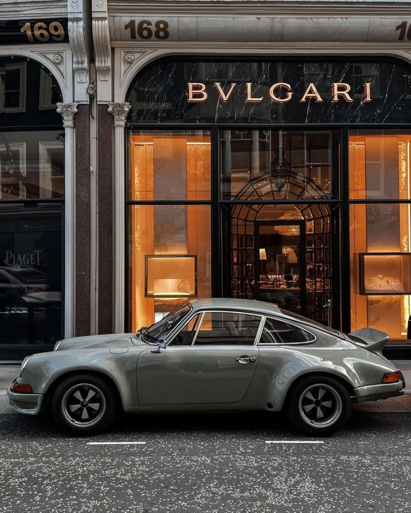 Classic grey Porsche parked outside Bulgari store with orange windows on Bond Street, one of London’s most famous shopping streets