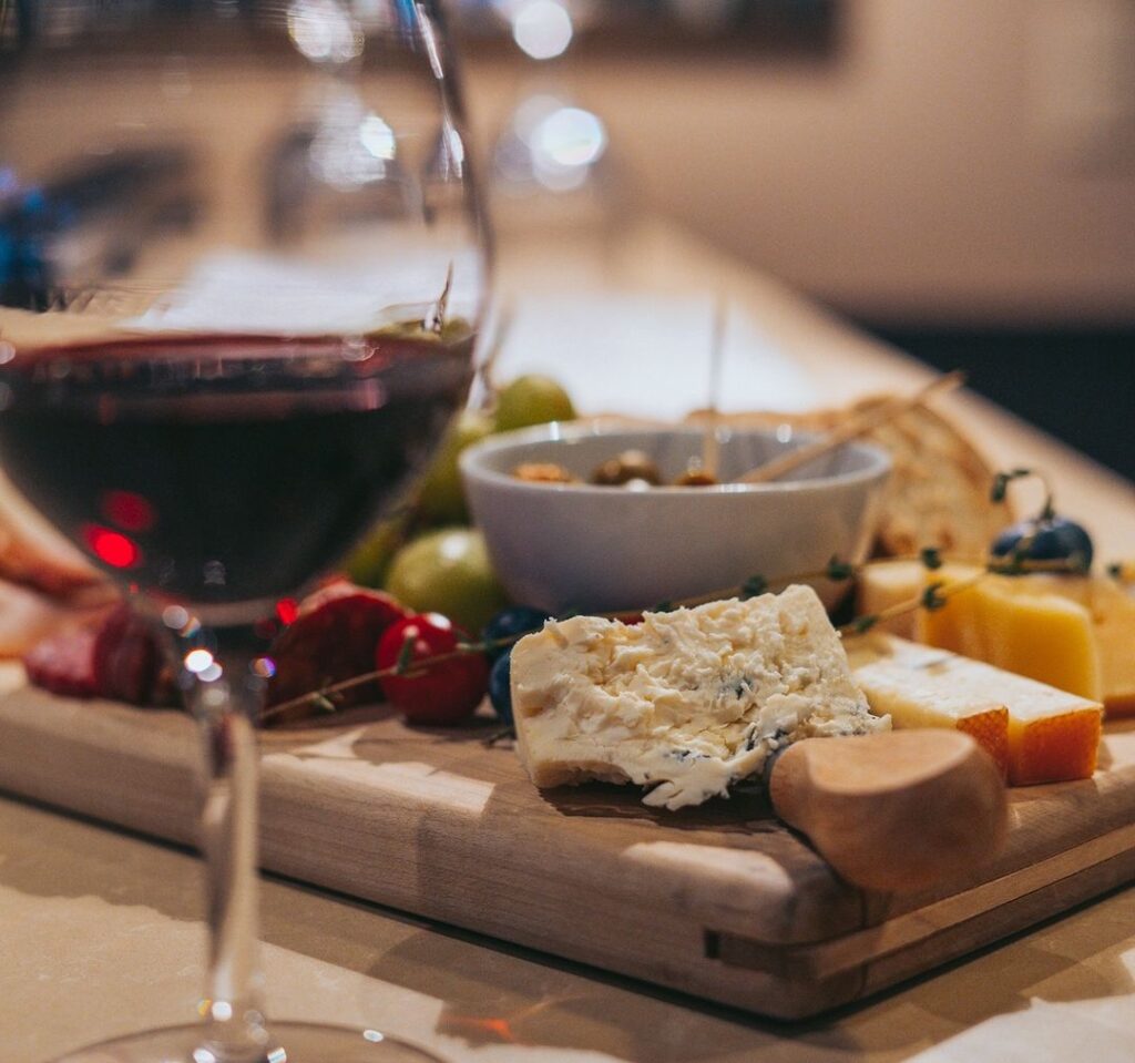 close up of red wine in a glass with a platter of cheese and fruit in the background