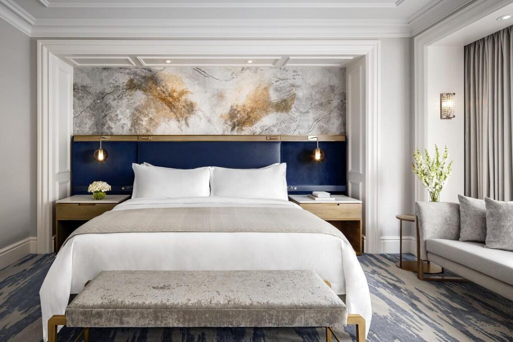 Blue, green and gold furnishings in an elegant hotel room at the St Regis hotel Toronto, grey covers drape a large king sized bed and light floods in