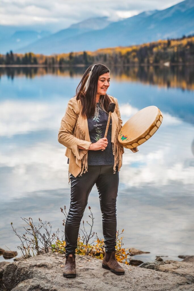 Cree Warrior Woman playing a traditional drum on the lake shore in Jasper Canada