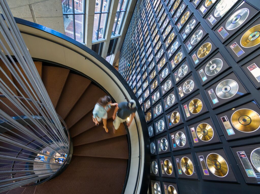 Stairs spiral down at the Nashville Country Music Hall of Fame, with two people looking at gold and sliver discs that adorn the walls