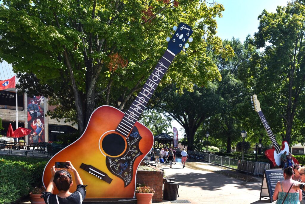 A huge brown and yellow guitar marks the entrance to the Grand Ole Opry in Nashville, USA, with trees and the opry house behind