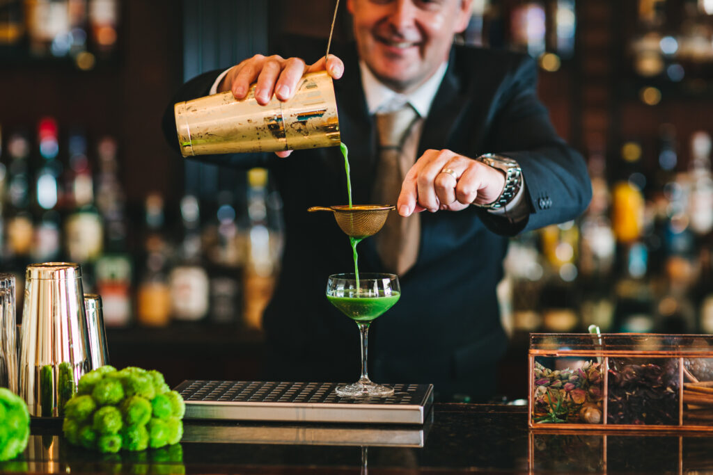 A master mixologist at the Hotel Esplanade Zagreb pours a bright green cocktail against the backdrop of the bar