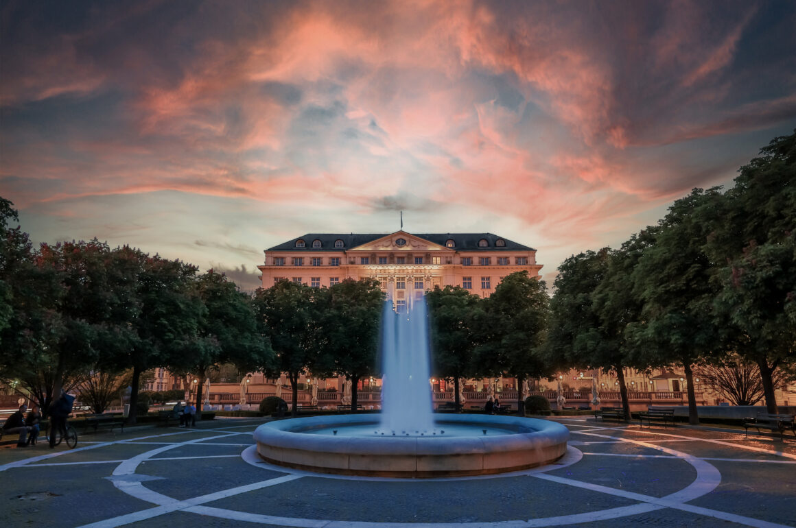 A sunset view of the Hotel Esplanade Zagreb with trees and a fountain in front