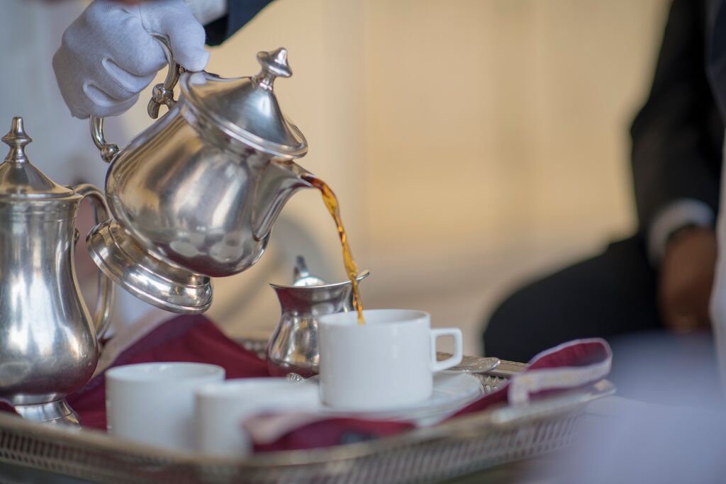 Gloved hands pouring tea into white cups on a tray