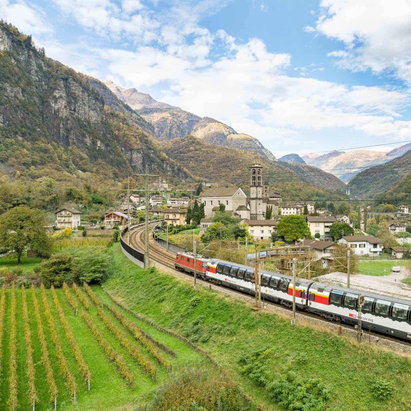 The Gotthard Panorama Express train travelling through town with mountains in background