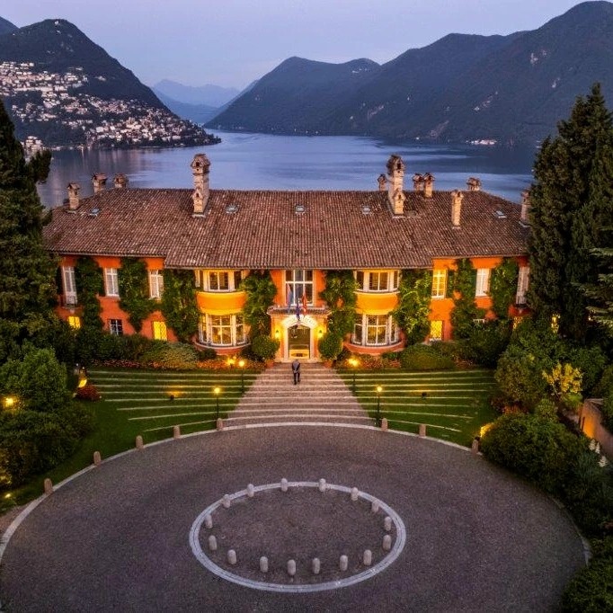 Aerial shot of Villa Principe Leopoldo at night with water and mountains in background 