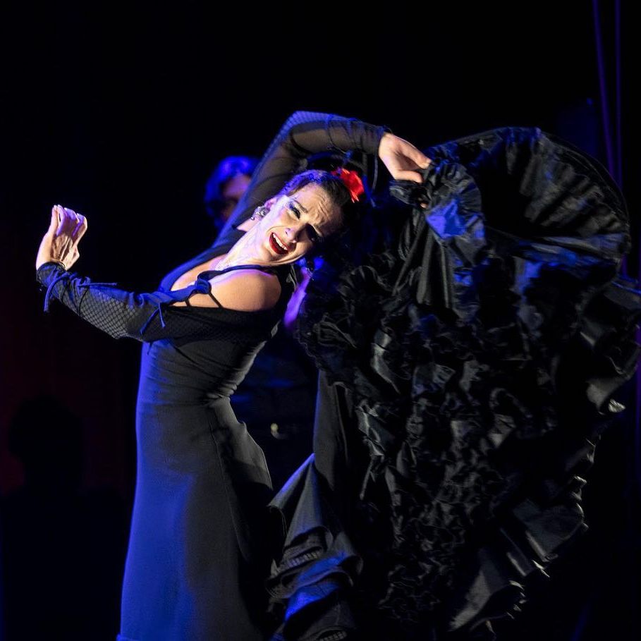 A flamenco dancer, dressed in black, performs with a concentrated look on her face