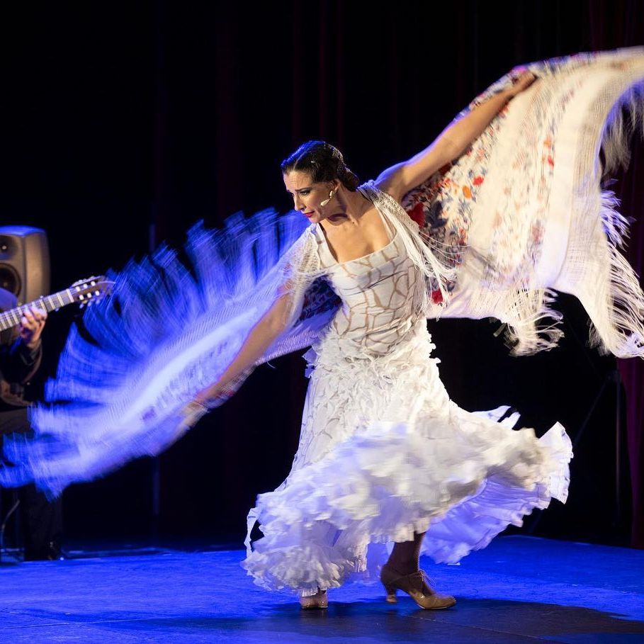 A flamenco dancer wearing white twirls on stage