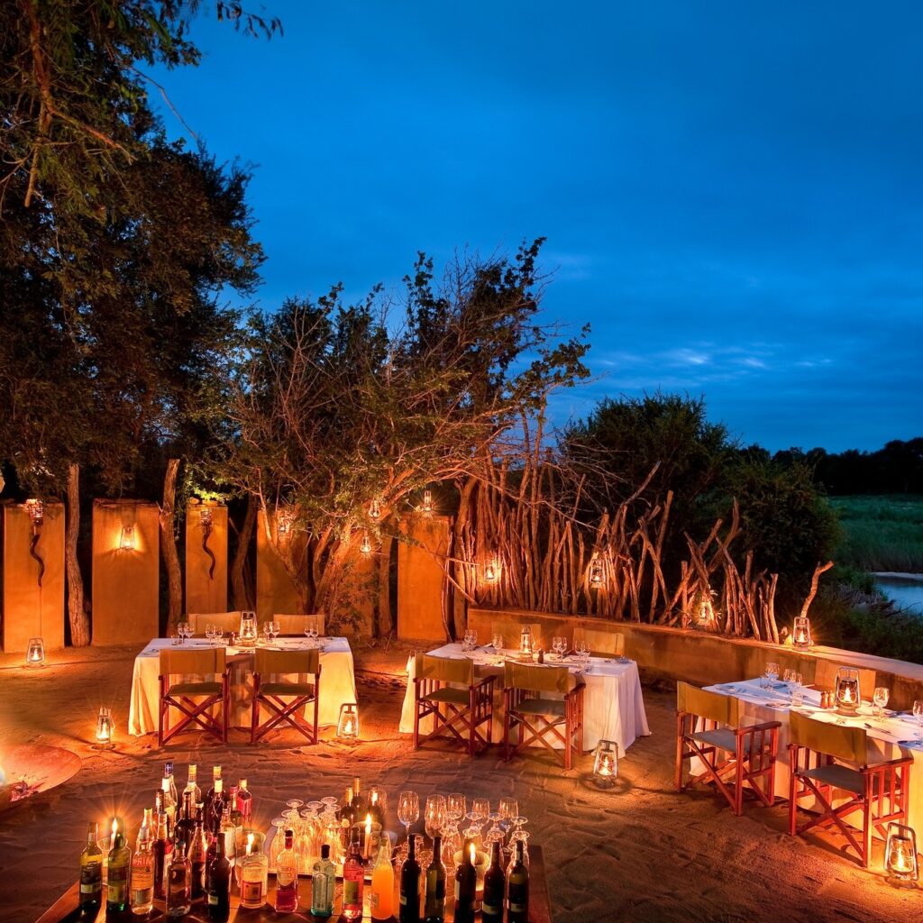 Tables are set with the glow of candles, outside on safari with a dark blue night sky and bushland behind