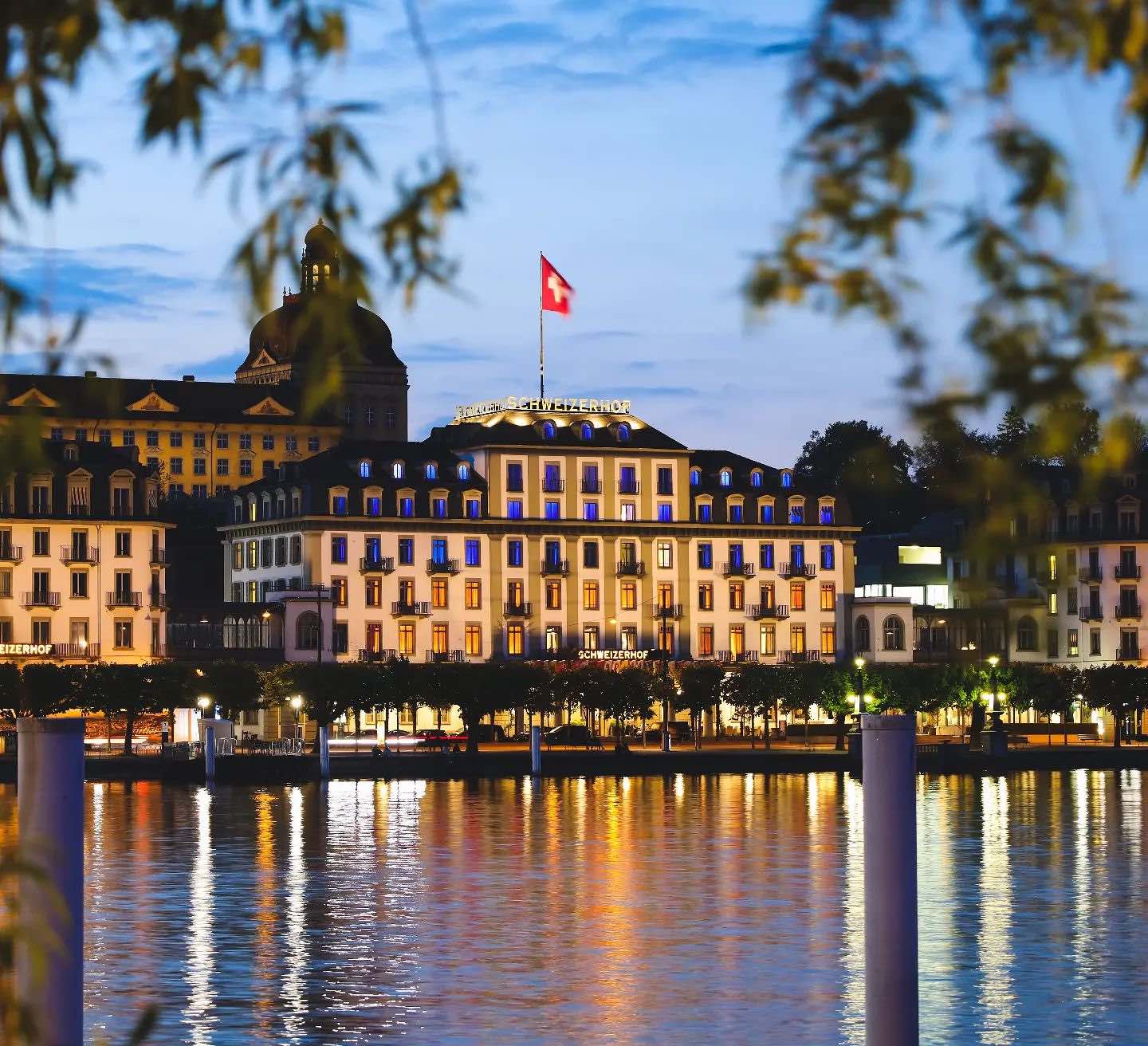 Hotel Schweizerhof Luzern lit up at night with body of water in foreground