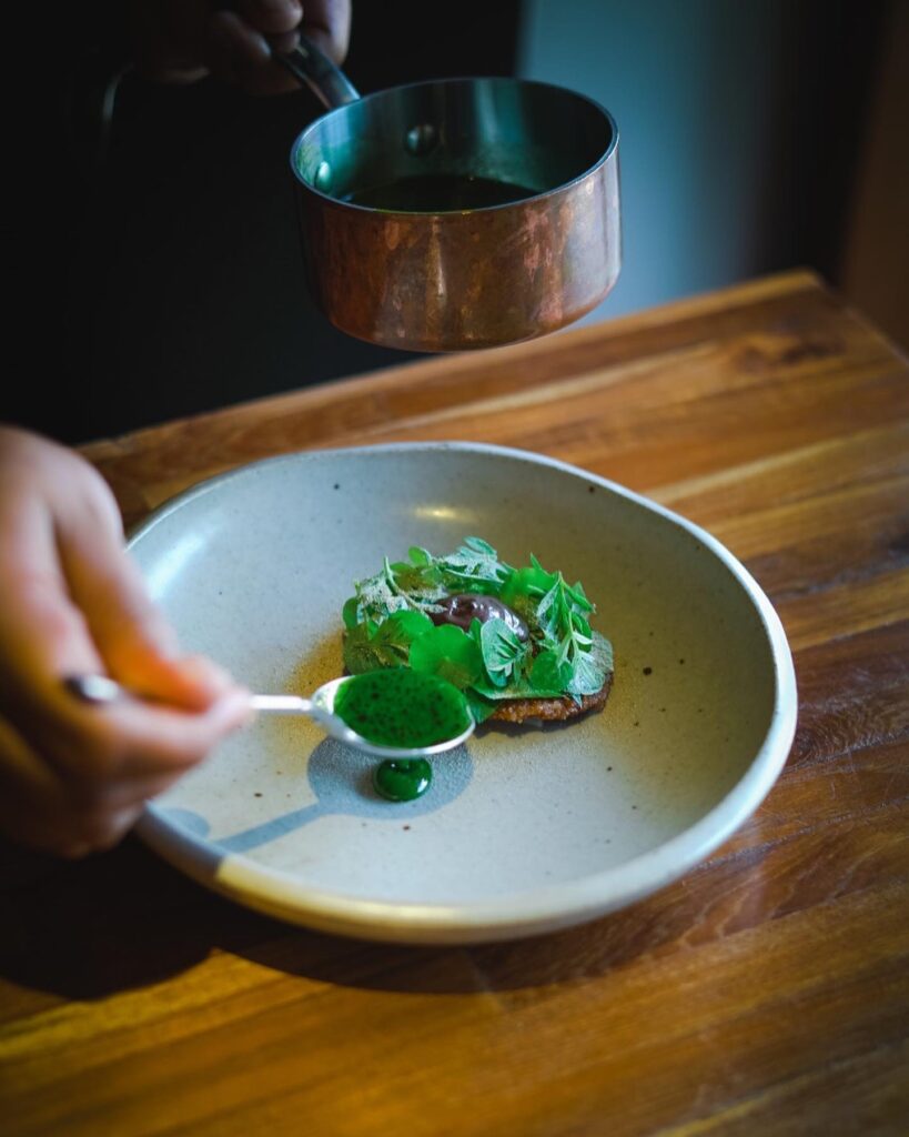 Chef pouring green sauce on a dish at locavore restaurant, Bali