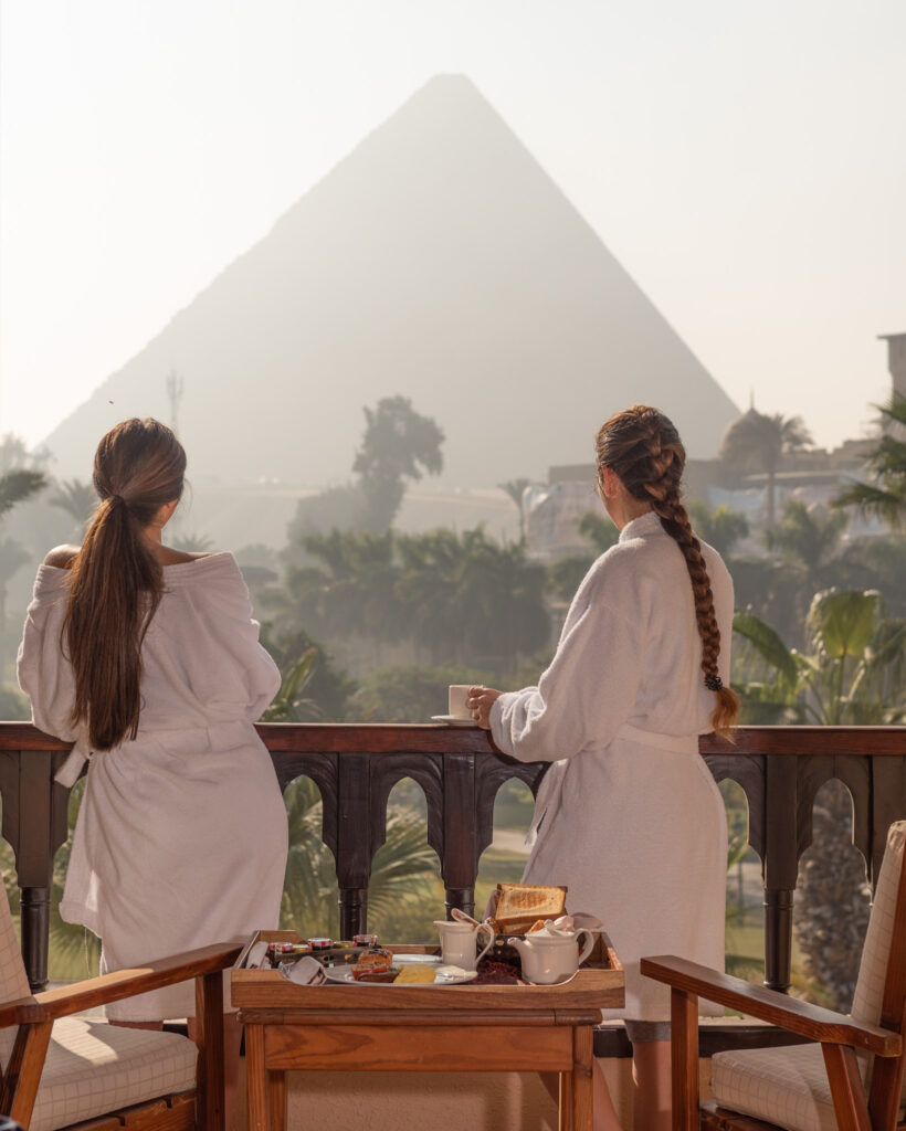 Two women standing on hotel balcony with a pyramid in background