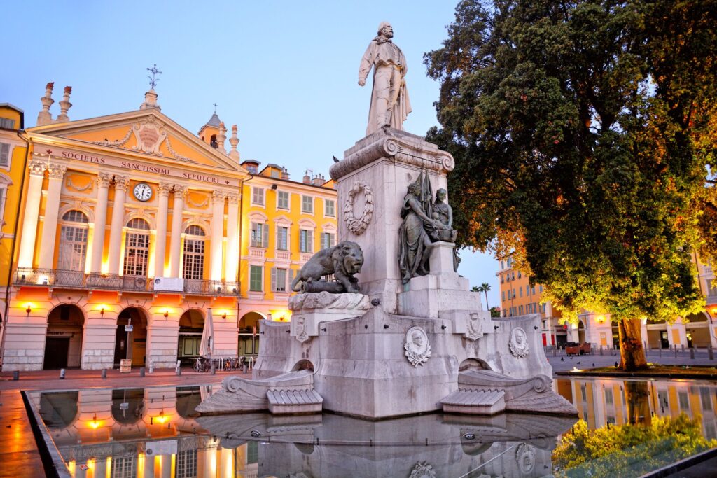 An ornate fountain stands in front of a peach coloured state building in Nice, Southern France
