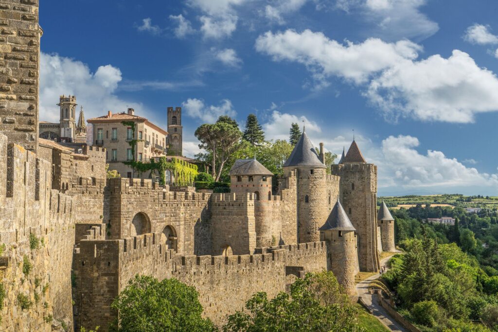 Ancient stone ramparts in Carcasonne, Southern France, with trees in front and a bright blue sky with white clouds