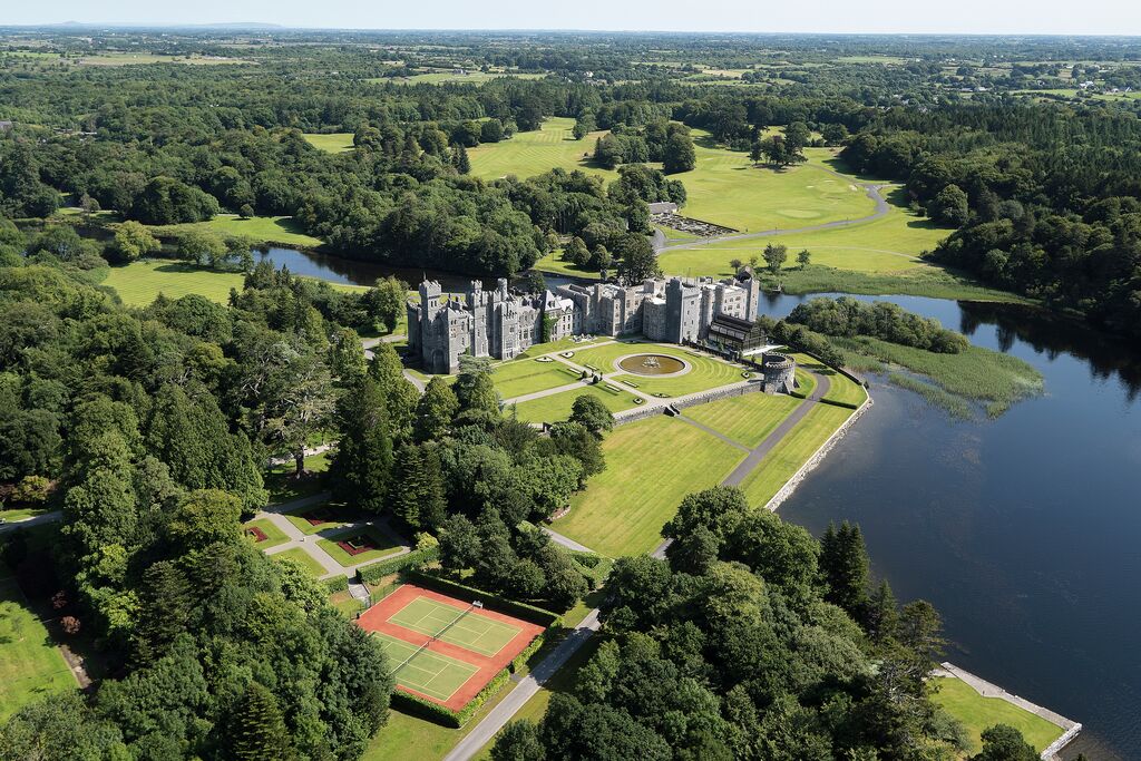 Aerial view of Ashford Castle hotel and grounds, with views stretching across green fields and woodland