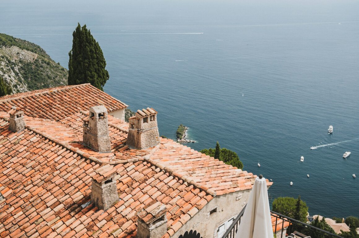 Image of terracotta tile-roofed house on top of a cliff overlooking the sea, with small boats visible on the water below