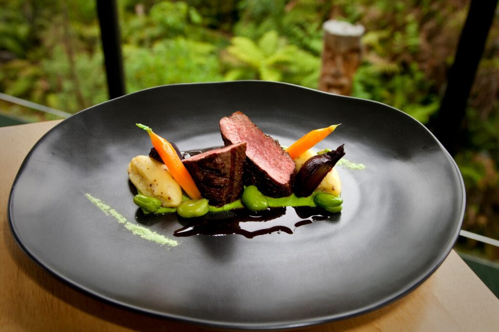 Photo of a black plate of artfully-prepared food, set against a background of foliage